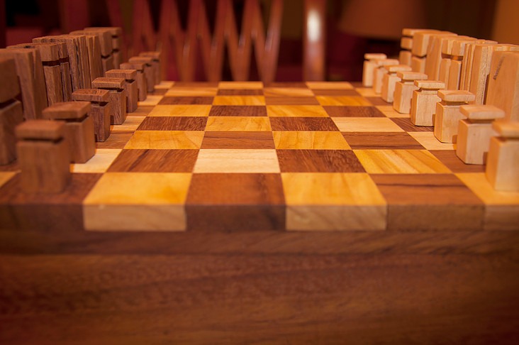 Eye-level view down the length of the board with pieces set up on both sides, showing the wood contrast