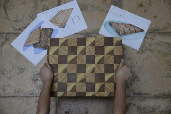 A finished checkerboard end-grain board next to its original design sketches